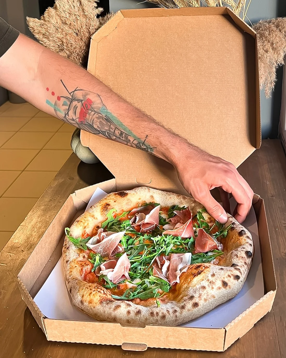 Pizza cu prosciutto și rucola, abia scoasă din cuptor, așezată în cutie